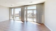 Located at 441 E Erie St in Milwaukee's vibrant harbor district, this three-bedroom, three-bathroom residence delivers a modern aesthetic with high-quality finishes throughout. The open-concept kitchen and living area serves as the heart of the home, where rich hardwood-style flooring flows beneath floor-to-ceiling windows and sliding glass doors that frame sweeping waterfront views of Milwaukee's marina and cityscape, flooding the space with abundant natural light.

The kitchen is outfitted with warm wood cabinetry paired with white upper cabinets, a striking marble-look island with generous counter space, textured tile backsplash, stainless steel appliances including a French door refrigerator, and a gas cooktop beneath a sleek range hood. The design balances functionality with contemporary style.

The primary bedroom is generously proportioned and features plush carpeting, neutral walls, and access to a dedicated walk-in closet with built-in shelving and drawers. Additional bedrooms offer carpeted floors and sliding wood-panel closet doors. The bathrooms are finished in a clean, modern palette featuring floating wood vanities, backlit mirrors, light wood-tone flooring, and a mix of walk-in glass showers and soaking tub configurations.