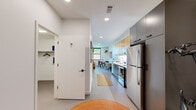 Located at 302 SE D St in Bentonville, Arkansas, this single-story unit showcases a clean, modern design with a well-organized open floor plan. The interior is finished with smooth, light-toned flooring throughout, crisp white walls, and recessed lighting that creates a bright, cohesive atmosphere.

The kitchen is a standout feature, outfitted with two-tone cabinetry combining warm wood upper cabinets and slate-gray lower cabinets, white quartz countertops, a subway tile backsplash, and stainless steel appliances including a refrigerator and range. A dedicated workspace area adjacent to the kitchen offers a compact desk setup, ideal for remote work.

The living area benefits from multiple black-framed windows that invite abundant natural light and views of surrounding greenery, lending the space an open, airy feel. The layout also accommodates a dining area, seamlessly connecting social and functional zones.

The bathroom features white tile walls, a tub-shower combination, and a wood-toned vanity with a white countertop. An in-unit laundry area houses a stacked washer and dryer alongside a hanging rod and shelving for added convenience. A closet near the entry provides additional storage.