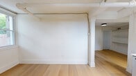 Located at 300 E 30th St in Baltimore's vibrant Charles Village neighborhood, this one-bedroom, one-bathroom unit offers a thoughtfully designed and efficiently laid-out living space. Throughout the home, light-toned hardwood floors create a warm, cohesive aesthetic that ties each room together seamlessly.

The main living area is characterized by crisp white walls, exposed overhead piping and beams painted white for a clean industrial touch, and a structural column that adds architectural character. A window allows natural light to filter in, enhancing the open and airy feel. A wall-mounted mini-split system provides convenient climate control.

The kitchen is a standout feature, equipped with deep navy cabinetry accented by brass hardware, white quartz countertops, a white subway tile backsplash, and a gold-toned pull-down faucet. Stainless steel appliances — including a gas range, dishwasher, and over-the-range microwave — complete this functional and stylish cooking space.

The bedroom is a quiet, well-proportioned room with light hardwood floors, crown molding, and a paneled white door. Built-in shelving nearby adds practical storage options.

The bathroom features marble-look tile flooring and a soaking tub with a shower curtain, finished in a clean all-white palette. Every detail of this unit reflects a modern, refreshed interior design.