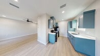 This thoughtfully designed single-floor unit offers a clean, modern aesthetic across two bedrooms, one bathroom, and a combined kitchen and living area. Light wood-look flooring runs throughout, creating a cohesive and airy feel that connects each room seamlessly.

The open-concept kitchen and living room is a standout feature, anchored by a striking galley-style kitchen outfitted with bold teal cabinetry, white countertops, black appliances — including a gas range and refrigerator — and a stainless steel sink. Upper and lower cabinets provide generous storage, while recessed lighting and a ceiling fan enhance both function and comfort. The adjacent living area benefits from natural light through multiple windows and shares the same ceiling fan, creating a bright, welcoming atmosphere.

Both bedrooms are well-proportioned and bright, each featuring ceiling fans, light-filled windows, and the same consistent wood-look flooring. The primary bedroom offers a comfortable footprint with access to natural light.

The full bathroom is finished with a tiled walk-in shower with a built-in niche, wood-look tile flooring, a white countertop vanity with teal cabinetry, and recessed lighting. A dedicated laundry area with washer/dryer hookups and overhead shelving adds practical convenience to the unit's well-rounded layout.