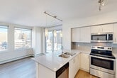 Located in Calgary's vibrant Beltline neighbourhood, this one-bedroom, three-bathroom unit offers a thoughtfully designed layout with a clean, modern aesthetic throughout. Light wood-style flooring and crisp white walls create a bright, cohesive feel across the entire space.

The open-concept kitchen and dining area is a standout feature, equipped with stainless steel appliances — including a refrigerator, electric range, and built-in microwave — white cabinetry reaching to the ceiling, a tiled backsplash, and a peninsula with a double sink and pendant lighting. Floor-to-ceiling windows flood the area with natural light and frame striking views of the Calgary skyline.

The bedroom is a well-proportioned retreat with a large window offering cityscape views, light flooring, and a built-in closet. Multiple additional closets are distributed throughout the unit, providing generous storage. The hallway connects the rooms efficiently, with a sliding closet panel adding to the streamlined design.

All three bathrooms are finished in white tile with soaker tub-and-shower combinations and chrome fixtures. Two dedicated laundry areas add further convenience. The overall ambiance is clean, contemporary, and functional — well-suited for urban living in one of Calgary's most walkable and connected communities.