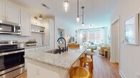 Located at 96 E Catawba St in Belmont, North Carolina, this single-floor residence offers a thoughtfully designed open-concept layout that seamlessly connects the kitchen, dining, and living areas. The kitchen is a standout feature, showcasing granite countertops, a large center island with bar seating, white shaker cabinetry with gold hardware, a classic subway tile backsplash, and stainless steel appliances. Pendant lighting above the island adds both function and style. Warm hardwood flooring flows throughout the entire residence, creating a cohesive and inviting atmosphere. The living room is bathed in natural light from oversized windows that frame views of the surrounding streetscape, and the open layout makes the space feel expansive and airy. The bedroom is a serene retreat, featuring large windows that bring in ample natural light. The bathroom is finished with granite-topped vanities, gold hardware accents, white tile surround, and hardwood-style flooring, and opens directly into a well-organized walk-in closet with built-in shelving. Throughout the residence, the consistent use of neutral tones, quality finishes, and modern fixtures creates a clean, contemporary aesthetic that is both functional and refined.