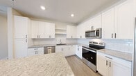 Located at 2300 N Broad St in Fuquay-Varina, NC, this thoughtfully designed single-story home offers three bedrooms, two bathrooms, and four closets across a comfortable, well-organized layout. The kitchen is a standout feature, showcasing white shaker cabinetry with matte black hardware, a classic subway tile backsplash, granite countertops, and stainless steel appliances including a range, microwave, and dishwasher. A large granite-topped island provides additional prep and storage space, while light wood-look flooring ties the area together seamlessly. The open living area adjoins the kitchen, featuring a built-in niche, neutral walls, and recessed lighting for a clean, modern aesthetic. The primary bedroom is generously sized with multiple windows that invite natural light and an en-suite bathroom featuring a long double-vanity with granite countertops, white cabinetry, and wood-look flooring. A spacious walk-in closet with full wire shelving systems offers excellent storage. The secondary bedrooms are carpeted and each equipped with ceiling fans and windows overlooking the neighborhood. The second bathroom includes a tub-shower combination, granite vanity, and wood-look flooring, maintaining the home's consistent, polished style throughout.