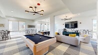 Located at 3801–3811 Howe St in Oakland, CA, this single-floor communal space offers a generously sized, open-plan layout encompassing a living room, dining room, and kitchen. The interior design is contemporary and cohesive, highlighted by a bold checkered carpet pattern in tones of gray, yellow, and cream that flows throughout the space, complemented by crisp white walls and modern pendant and sputnik-style light fixtures.

The living area features a pool table as a central focal point, alongside comfortable lounge seating including sofas and swivel chairs accented with yellow throw pillows. A wall-mounted television and built-in banquette seating with dual circular mirrors add depth and function. A distinctive abstract graphic wall treatment runs along the perimeter, lending an artistic character to the space.

The dining area is anchored by a round wood table with upholstered chairs and benefits from abundant natural light through floor-to-ceiling sliding glass doors that open to a spacious outdoor terrace with open views of the Oakland skyline and surrounding greenery.

The kitchen is fully equipped with stainless steel appliances, a professional-grade range, subway tile backsplash, gray cabinetry, and a large granite-topped island with bar seating, making it well-suited for group gatherings and events.