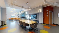 This contemporary amenity center is designed to offer a diverse range of social, recreational, and wellness facilities across a single, thoughtfully laid-out floor. The main lounge area serves as the heart of the space, featuring a sleek linear fireplace set beneath a wall-mounted TV framed by textured wave-panel surrounds, complemented by comfortable seating and abundant natural light from surrounding windows. Adjacent to the lounge, a conference and meeting area provides a large wooden table with ample seating, striking geometric pendant lighting overhead, and a mounted display screen — ideal for collaborative gatherings. The game room offers a spacious, open layout with a billiards table, ping pong table, colorful hexagonal floor accents, exposed ductwork ceilings, and curated wall art, creating an energetic and social atmosphere. A dedicated private screening room features tiered rows of black leather recliner-style seating, acoustic panel walls, a deep red ceiling, and projector equipment for an immersive cinema experience. The fitness facilities are exceptional, comprising a main gym with high ceilings, large glass garage-style doors that flood the space with natural light, and a full array of strength and cardio equipment. A separate yoga and group exercise studio features wood-look flooring, exercise mats, stability balls, and its own oversized glass garage door opening to the outdoors, creating a bright and airy environment for movement and wellness.