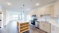 Located at 250 Plaza Circle in Mundelein, IL, this well-appointed single-floor residence offers four bedrooms, two bathrooms, and a thoughtfully designed open-concept layout. The kitchen and living area serve as the heart of the home, showcasing light wood cabinetry, a classic white subway tile backsplash, stainless steel appliances, and a central island with built-in shelving accented by globe pendant lights. Rich hardwood-style flooring flows throughout the main living spaces, adding warmth and continuity. The living room is bathed in natural light through large windows with horizontal blinds, offering open outdoor views. The four bedrooms feature a mix of hardwood-style and plush carpeted flooring, with clean white walls providing a neutral, versatile canvas. The primary bedroom is generously sized, offering ample space for a variety of furniture arrangements. Two closets provide practical storage solutions, including a walk-in closet with wire shelving. The two bathrooms are finished in a contemporary style, with one featuring a glass-enclosed walk-in shower adorned with elegant linear tile surround and a rain showerhead. A dedicated entrance, hallway, and additional closet space complete this functional and modern layout.