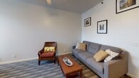This single-floor residence offers a thoughtfully organized layout designed for comfortable everyday living. The kitchen is equipped with warm honey-toned wood cabinetry, white appliances including a gas range and refrigerator, recessed lighting, and tile flooring — providing ample counter space and storage in a U-shaped configuration. Adjacent to the kitchen, the dining area features elegant wall sconce lighting that creates a warm ambiance, complemented by framed artwork and a classic wooden dining table. The living room is carpeted and offers a relaxed atmosphere with a ceiling fan, a grey sofa, and decorative framed prints on the walls. The space includes multiple bedrooms, each carpeted and bathed in natural light through large windows with outdoor views of surrounding trees. One bedroom features a mirrored sliding closet and decorative artwork, while others accommodate multiple beds and include dressers and accent chairs. The two full bathrooms are finished in light tones with pedestal sinks, mirrored medicine cabinets, and tub-shower combinations with decorative curtains, giving each a clean and classic feel. Throughout, the residence maintains a cohesive, neutral palette with light grey and white walls that contribute to a bright, inviting atmosphere.