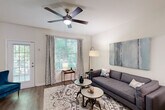This two-story, two-bedroom, three-bathroom home in East Point, Georgia offers a thoughtfully designed layout spread across two floors. The main level features an inviting living room with hardwood-style flooring, a ceiling fan, and large windows that flood the space with natural light and offer views of surrounding greenery. A standout geometric accent wall in teal, taupe, and white anchors the dining area, adding a bold, artistic focal point adjacent to the staircase. The kitchen is well-appointed with white shaker-style cabinetry, granite-look countertops, and a full suite of stainless steel appliances, including a refrigerator, range, and over-the-range microwave. A convenient half bathroom completes the main level. Upstairs, the primary bedroom offers a comfortable, carpeted retreat with ample space, while the second bedroom features bright windows with garden views and plush carpet. Both upper-level bathrooms are finished with granite-top vanities and tiled tub-shower combinations. Two closets provide practical storage throughout. The home combines neutral tones with modern accents, creating a clean, contemporary ambiance suitable for a variety of lifestyles.