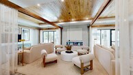 Located on College Pointe Court in Fort Myers, Florida, this single-floor lobby space offers a refined coastal aesthetic across a generously sized footprint. The entrance welcomes visitors through dramatic floor-to-ceiling black-framed glass doors, opening to a light-filled corridor with warm wood-paneled ceilings and crisp white walls. A built-in bench with a subtly textured fluted accent wall provides an inviting seating nook near the entry.

The centerpiece of the space is an expansive communal kitchen and gathering area, anchored by a substantial white quartz island accommodating numerous bar stools. Dome pendant lights hang from a recessed wood-clad ceiling, while open shelving and a full-service coffee station line the back wall. A wall-mounted display screen adds a functional, modern touch.

Adjacent to the kitchen, a sophisticated lounge features exposed wood beam ceilings, oversized cream-toned seating, and a sleek linear fireplace, all framed by large windows that draw in abundant natural light and outdoor views.

A dedicated conference room offers a patterned tile floor, a dark wood boardroom table, globe pendant lighting, a mounted display, and gallery-style framed artwork along the walls, making it ideal for professional meetings. Throughout, the design seamlessly blends warm natural materials with contemporary finishes.