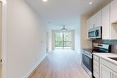 Located at 421 Broadway St in Asheville, NC, this one-bedroom, one-bathroom residence offers a thoughtfully designed single-floor layout that maximizes every square foot. Light wood-tone flooring runs throughout the unit, creating a warm, cohesive aesthetic from room to room.

The open living and kitchen area serves as the heart of the home. The kitchen is equipped with stainless steel appliances — including a range, microwave, refrigerator, and dishwasher — complemented by white shaker cabinetry, granite-style countertops, and a tasteful tile backsplash. Track lighting and recessed fixtures illuminate the space efficiently. A large sliding glass door opens to a private balcony, flooding the living area with natural light and offering leafy outdoor views. A ceiling fan adds comfort to the open living zone.

The bedroom is a calm, well-lit retreat featuring a ceiling fan, a wide window with views of surrounding greenery, and clean white walls. An adjacent closet provides dedicated storage.

The bathroom features light gray cabinetry with granite-style countertops and direct access to the closet. The unit's entry area includes additional storage and a modern front door. Clean lines, a neutral palette, and contemporary finishes define the overall ambiance of this well-appointed Asheville residence.
