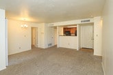 This single-floor residence at 9100 San Mateo Blvd NE offers a well-designed open-concept layout where the kitchen, dining, and living areas flow seamlessly together. The kitchen is a standout feature, showcasing dark wood-grain cabinetry paired with light quartz countertops, black appliances including a gas range and built-in microwave, and a central island with an integrated sink and pendant lighting overhead. Track lighting throughout the kitchen and dining area ensures excellent illumination. A dedicated dining nook adjacent to the kitchen comfortably accommodates a round table and chairs. The living room benefits from large windows and a glass door that invite natural light and provide outdoor access, creating an airy, welcoming atmosphere. Light wood-style flooring runs throughout the main living areas, transitioning to plush carpet in the bedrooms. Each bedroom is comfortably proportioned, featuring ceiling fans, windows with natural light, and neutral tones. The primary bathroom impresses with a dual-sink vanity, dark cabinetry, light countertops, and large mirrors, while a secondary bathroom offers similarly clean, modern finishes. Overall, the space maintains a contemporary aesthetic with cohesive design elements throughout.