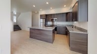 This three-floor space is designed with a clean, contemporary aesthetic that balances functionality and modern style. The kitchen serves as a central highlight, featuring dark wood cabinetry, granite countertops, a substantial center island, and a full suite of stainless steel appliances including a refrigerator, range, and built-in microwave. Light hardwood flooring flows throughout the kitchen and main living areas, complementing the neutral white walls and recessed lighting overhead. Large windows in the living area allow generous natural light to fill the space while offering views of the surrounding neighborhood.

The bedrooms are finished with plush carpet and feature vaulted ceilings that add an airy sense of height. Bright windows provide additional natural light and neighborhood views. Carpeted hallways connect the upper-floor rooms, maintaining a cohesive and comfortable feel.

Bathrooms are finished consistently with granite-topped dark wood vanities and light hardwood-style flooring, mirroring the kitchen's design language. One bathroom includes a full tub-shower combination. A dedicated laundry area houses a stacked washer and dryer unit alongside built-in shelving for storage. A half bath with a window provides added convenience on a separate floor.