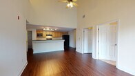 This two-floor residence offers a well-designed layout that balances open communal spaces with private retreats. The heart of the home is an open-concept kitchen and living area anchored by rich, dark hardwood flooring that flows throughout the main level. The kitchen is equipped with warm maple cabinetry, dark granite-style countertops, black appliances including a refrigerator, range, and built-in microwave, and a central island with a sink that doubles as a breakfast bar. Track lighting illuminates the kitchen, while a ceiling fan overhead completes the living area. A dramatic double-height ceiling over the living space creates an expansive, airy ambiance, with a lofted second floor visible above, accessible via the upper level. Bedrooms feature plush carpeting, ceiling fans, and windows that bring in natural light and outdoor greenery views. The bathroom includes a warm wood vanity with ample cabinet storage, a large mirror, and a full tub-shower combination with tiled surround. A dedicated laundry area with a full-size washer and dryer and an in-unit water heater adds everyday convenience. Throughout, the space maintains a clean, neutral palette that offers a versatile backdrop for any style.