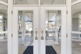 Located at 2000 Cascade Ridge Drive in Jackson, Michigan, this thoughtfully designed single-floor clubhouse offers a refined and functional layout across a comfortable footprint. The entrance greets visitors through elegant full-glass double doors framed in crisp white, with transom windows above that flood the interior with natural light from the moment you arrive.

The combined kitchen and living room serves as the heart of the space. The kitchen features grey shaker-style cabinetry, stainless steel appliances, a striking geometric patterned tile backsplash, and a sweeping curved island with a quartz countertop and bar seating beneath a stylish drum pendant light. Sage green accent walls and light wood-look tile flooring lend a fresh, modern character throughout.

The living room is a standout, boasting soaring ceilings, floor-to-ceiling windows, and glass doors that open to views of an outdoor pool area. A double-sided fireplace anchors the room, while plush seating arrangements and patterned area rugs create an inviting, communal atmosphere.

The office offers a quiet retreat, complete with built-in bookshelves, a round meeting table, and natural light from oversized windows. The exercise room provides a dedicated space for fitness, and a connecting hallway ties all areas together seamlessly. The overall ambiance is clean, bright, and contemporary.