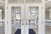 Located at 2000 Cascade Ridge Drive in Jackson, Michigan, this thoughtfully designed single-floor clubhouse offers a refined and functional layout across a comfortable footprint. The entrance greets visitors through elegant full-glass double doors framed in crisp white, with transom windows above that flood the interior with natural light from the moment you arrive.

The combined kitchen and living room serves as the heart of the space. The kitchen features grey shaker-style cabinetry, stainless steel appliances, a striking geometric patterned tile backsplash, and a sweeping curved island with a quartz countertop and bar seating beneath a stylish drum pendant light. Sage green accent walls and light wood-look tile flooring lend a fresh, modern character throughout.

The living room is a standout, boasting soaring ceilings, floor-to-ceiling windows, and glass doors that open to views of an outdoor pool area. A double-sided fireplace anchors the room, while plush seating arrangements and patterned area rugs create an inviting, communal atmosphere.

The office offers a quiet retreat, complete with built-in bookshelves, a round meeting table, and natural light from oversized windows. The exercise room provides a dedicated space for fitness, and a connecting hallway ties all areas together seamlessly. The overall ambiance is clean, bright, and contemporary.