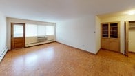 Located at 1901 E Capitol Dr in Shorewood, WI, this single-floor unit showcases a consistent design language anchored by warm parquet wood flooring that extends throughout the living spaces and bedrooms. The open layout connects the main living area to adjacent rooms, creating a functional and cohesive floor plan.

The generously sized living room benefits from natural light streaming through multiple windows fitted with blinds, and is equipped with a wall-mounted HVAC unit and baseboard heating. A pass-through counter connects the living area to the kitchen, enhancing the sense of openness between spaces.

The kitchen features white upper cabinetry with wood trim, a white electric range, refrigerator, and ample counter space. Light-toned tile flooring completes the practical, functional design of the room.

The bedroom offers parquet flooring, two windows that invite natural light and views of surrounding greenery, baseboard heating, and a closet with bi-fold louvered doors providing organized storage.

The bathroom includes a wide vanity with a light-colored countertop, flanked by full-length mirrors that amplify the sense of space. A window above the vanity provides natural ventilation. The separate tiled bath area includes a soaking tub and wall-mounted heater, with clean white tile flooring throughout.