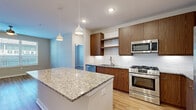This well-designed single-floor residence showcases a contemporary aesthetic carried consistently throughout its living spaces. The kitchen serves as a central highlight, featuring a large granite-topped island illuminated by stylish pendant lights. Warm-toned wood cabinetry pairs with a white subway tile backsplash, while a full suite of stainless steel appliances—including a gas range, built-in microwave, French door refrigerator, and dishwasher—ensures full functionality. Recessed lighting and an open layout connect the kitchen seamlessly to the living areas.

Light hardwood-style flooring flows throughout the unit, lending warmth and visual continuity. The living areas are bright and open, benefiting from large windows fitted with horizontal blinds that allow natural light while maintaining privacy. Ceiling fans are present in the bedrooms and living spaces, adding comfort.

The bathroom is well-appointed with a granite-topped double vanity, wood cabinetry, framed mirrors, and a glass-enclosed walk-in shower, all set on matching hardwood-style flooring. Storage is thoughtfully addressed through generously sized walk-in closets outfitted with built-in shelving, hanging rods, and drawer units. Additional louvered closet doors are visible near the kitchen area, providing further storage options.