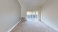 This single-story residence offers a thoughtfully designed layout with a warm and comfortable ambiance throughout. The living area is generously proportioned, featuring soft wall-to-wall carpeting, crown molding, and a sliding glass door fitted with vertical blinds that opens to a private balcony overlooking lush greenery, allowing natural light to fill the space. A wall-mounted air conditioning unit ensures year-round comfort in this main living area.

The kitchen is well-appointed with white cabinetry, dark granite countertops, stainless steel appliances including an electric range and dishwasher, and tile flooring. A window with vertical blinds provides natural light and ventilation. Crown molding details carry throughout, lending a polished finish to the space.

The bedrooms are carpeted and bright, each featuring crown molding and windows dressed with vertical blinds that bring in natural light. Mirrored sliding closet doors are a standout feature, adding depth and a sense of openness to the rooms. A ceiling fan is present in one of the bedroom or adjoining areas, contributing to the comfortable atmosphere.

The bathroom is finished with diagonal tile flooring, a dark granite vanity countertop, and a full tub-shower combination, offering a clean and functional design. Overall, this residence presents a cohesive, well-maintained interior with classic detailing throughout.