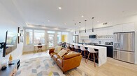 Located in the Capitol Hill neighborhood of Washington, DC, this thoughtfully designed single-floor residence offers an impressive eight bedrooms and five bathrooms across a spacious, well-appointed layout. The open-concept living and kitchen area serves as the heart of the home, showcasing light hardwood flooring, recessed lighting, and large windows that flood the space with natural light and neighborhood views. The chef's kitchen features two-tone cabinetry — white uppers paired with dark lower cabinets — a dramatic waterfall quartz island with bar seating, stainless steel appliances, and sleek pendant lighting. The adjoining living room provides a comfortable retreat with access to the patio. Three well-proportioned hallways connect the eight bedrooms, each offering bright windows with tree-lined or neighborhood views and clean, minimalist finishes. The five bathrooms are consistently styled with white subway tile, dark marble-look flooring, matte black hardware, and floating white vanities. Louvered barn-style closet doors add a distinctive architectural touch throughout the corridors. The overall aesthetic is clean, modern, and cohesive, making this a well-suited property for shared or co-living arrangements in the heart of DC.
