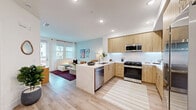 Located at 1205 Aviara Parkway in Carlsbad, CA, this thoughtfully designed one-bedroom, one-bathroom residence offers a bright and modern living experience on a single floor. The open-concept kitchen and living room serve as the heart of the home, featuring warm natural wood cabinetry, a striking marble-look quartz waterfall island with bar seating, stainless steel appliances including a gas range, built-in microwave, and French door refrigerator. Light wood-tone flooring flows throughout, complementing the soft, neutral color palette. The living area is filled with natural light from large windows and a glass-paned door that opens to a private balcony, creating a seamless indoor-outdoor connection. The bedroom offers a cozy retreat with a bold accent wall, a ceiling fan, and direct access to a spacious walk-in closet with built-in shelving. The full bathroom features neutral tile flooring, a wood-toned vanity with a white countertop, and a wood-paneled storage cabinet. A dedicated laundry area houses a stacked full-size washer and dryer for added convenience. Recessed lighting throughout the home enhances the clean, contemporary aesthetic of this well-appointed Carlsbad residence.
