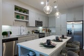 Located at 10820 Abbotts Bridge Rd in Johns Creek, GA, this single-floor residence showcases a thoughtfully designed layout with contemporary finishes throughout. The kitchen is a standout feature, equipped with crisp white shaker-style cabinetry, a classic subway tile backsplash, granite countertops, stainless steel appliances, and a generous central island with seating — ideal for both everyday cooking and casual entertaining. Rich dark hardwood-style flooring flows through the main living areas, complemented by recessed lighting and elegant pendant fixtures. The living room is bright and welcoming, offering floor-to-ceiling windows with transom details that invite abundant natural light and provide views to the outdoors, framed by stylish drapes. The bedrooms are carpeted for comfort, each offering a serene retreat. The primary suite includes a spacious walk-in closet with extensive wire shelving for organized storage. The bathrooms are finished with large-format tile flooring, granite-topped vanities, and glass-enclosed showers, conveying a clean, spa-like aesthetic. Throughout the home, neutral wall tones and modern hardware create a cohesive, refined atmosphere well-suited to contemporary living in the heart of Johns Creek.