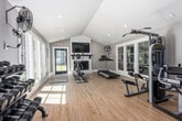 Located at 701 Crest Valley Way in Birmingham, Alabama, this dedicated exercise room delivers a comprehensive fitness environment within a bright, thoughtfully designed space. The room is defined by striking vaulted ceilings with recessed lighting, which create an open, airy atmosphere that enhances the sense of scale. Light hardwood flooring runs throughout, contributing to the clean, modern aesthetic.

Large windows along the walls flood the interior with natural light, offering views of the surrounding greenery and keeping the space feeling fresh and energizing. A white-painted fireplace serves as a focal point on one wall, topped with a wall-mounted television — a practical feature for entertainment during workouts.

The fitness setup is diverse and well-organized. Cardio equipment includes a treadmill and an elliptical/rowing machine, while a multi-station cable weight machine supports strength training. A dedicated dumbbell rack provides a full range of free weights, and a shiplap accent wall serves as a functional ball storage display, holding an assortment of medicine balls and stability balls alongside a stretching mat rack. A large floor fan ensures ventilation and comfort during intense sessions.

Natural light, vaulted ceilings, and a versatile equipment layout make this exercise room a functional and inviting space for a thorough fitness routine.