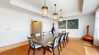 Located at 597 Westport Ave in Norwalk, CT, this refined single-floor space offers a thoughtfully designed layout across three distinct areas. The centerpiece is a spacious formal dining room accommodating a large rectangular conference-style table surrounded by upholstered chairs with botanical-print fabric. Three elegant bronze pendant lights hang overhead, while wainscoting and crown molding lend classic architectural character. A striking triptych bird artwork adorns one wall, and floor-to-ceiling sheer curtains filter abundant natural light from large windows that offer views of the surrounding greenery. Rich hardwood floors flow throughout and are complemented by a warm-toned area rug beneath the dining table. The fully equipped kitchen features mixed cabinetry in cream and dark walnut tones, dark granite countertops, a stainless farmhouse sink, stainless steel appliances, and globe pendant lighting above a central island. Warm hardwood floors and a geometric tile backsplash add texture and depth. A separate lounge area provides an intimate retreat, complete with a marble-surround fireplace topped by an oval mirror, a round dining table with a candle chandelier, and a corner library with floor-to-ceiling built-in bookshelves and comfortable seating — ideal for relaxed gathering or quiet reflection.