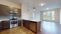 This well-designed single-floor residence offers a thoughtful layout that balances open communal spaces with comfortable private quarters. The heart of the home is the kitchen, which showcases rich dark-stained cabinetry, a classic subway tile backsplash, and a full suite of stainless steel appliances including a refrigerator, range, built-in microwave, and dishwasher. A generous center island with a white quartz-style countertop and undermount sink doubles as a casual dining and prep space, illuminated by a pair of stylish pendant lights that add a modern touch. The kitchen flows seamlessly into the adjacent living area, which benefits from natural light streaming through large windows with views of the surrounding neighborhood. Warm hardwood-style flooring runs throughout the main living spaces, lending the home a cohesive and inviting feel. The bedrooms are spacious and bright, each featuring large windows, hardwood-style floors, wall-mounted climate control units, and generous closet storage. The bathrooms are finished with coordinating dark wood vanities, white countertops, tile flooring, and well-lit mirrors, reflecting the same attention to detail found throughout the residence. Overall, the space presents a clean, contemporary aesthetic with quality finishes at every turn.