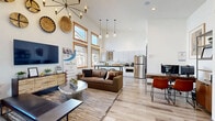 This 500 square foot space in Bend, Oregon showcases a thoughtfully designed open-concept layout. The centerpiece is an impressive floor-to-ceiling stone fireplace, adding a rustic touch to the otherwise modern aesthetic. High ceilings create a sense of spaciousness, while large windows flood the area with natural light and offer views of the surroundings.

The living area features comfortable seating, including a built-in bench beneath the windows, complemented by a sleek coffee table. Decorative woven baskets adorn the walls, adding texture and visual interest. The adjacent dining space is furnished with a contemporary table and chairs, suitable for both meals and work.

The kitchen, while compact, is well-equipped with white cabinetry, quartz countertops, and stainless steel appliances. A dedicated coffee station and ample counter space make it functional for daily use. Throughout the space, light wood flooring unifies the design and enhances the bright, airy atmosphere.

Thoughtful details such as modern light fixtures, carefully curated artwork, and strategically placed plants contribute to the overall cohesive and inviting ambiance of this efficiently designed space.