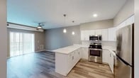 This single-floor residence offers a thoughtfully designed open-concept layout that seamlessly connects the kitchen and living areas. The kitchen is a standout feature, showcasing crisp white shaker cabinetry, a suite of stainless steel appliances including a refrigerator, electric range, microwave, and dishwasher, and a generous peninsula with a bright white countertop that provides additional workspace and casual seating. Elegant pendant lights hang above the peninsula, complementing the recessed lighting throughout. Wood-look plank flooring anchors the kitchen and living space, adding warmth to the contemporary aesthetic. The living area benefits from a ceiling fan and access to a patio or balcony via a sliding glass door, inviting natural light into the open space. The bedrooms are finished with plush carpet flooring, neutral taupe walls, ceiling fans, and windows with blinds that provide a comfortable, restful atmosphere. The bathroom features a wide vanity with a white countertop and undermount sink, a large mirror, and tiled accents, offering a clean and functional design. Throughout the residence, neutral tones and modern finishes create a cohesive and inviting ambiance.