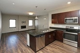 This single-floor residence offers a well-designed layout with a cohesive contemporary aesthetic. The kitchen serves as a functional centerpiece, outfitted with rich dark espresso cabinetry, dark granite countertops, and a full suite of stainless steel appliances including a side-by-side refrigerator with water dispenser, electric range, and built-in microwave. Wood-look plank flooring runs throughout the kitchen and connects seamlessly to adjacent living areas, adding warmth to the space.

The unit includes multiple bedrooms, each finished with plush carpeting and individual windows fitted with horizontal blinds, allowing natural light while maintaining privacy. One bedroom features a ceiling fan and a wall-mounted TV bracket, offering added convenience.

Two bathrooms serve the unit. The primary bathroom includes dark espresso cabinetry topped with a dark granite countertop, an undermount sink, a large mirror, and a separate water closet. A second bathroom features tile flooring and a full soaking tub with shower surround.

A dedicated laundry room with wood-look flooring houses a full-size top-load washer and dryer alongside wire shelving for additional storage, rounding out this thoughtfully arranged residence.