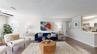 This single-story residence offers a thoughtfully arranged floor plan with distinct living, dining, kitchen, and sleeping areas connected by wood-look flooring throughout the main spaces. The living room serves as the heart of the home, featuring a textured ceiling, a ceiling fan, and a wide window that invites natural light. The open layout provides generous room for seating arrangements and flows seamlessly toward the entryway.

The galley-style kitchen is efficiently designed with white cabinetry, light quartz countertops, a double-basin sink, and stainless steel appliances including a refrigerator, range, microwave, and dishwasher. A hexagonal tile backsplash adds a decorative accent alongside ample upper and lower cabinet storage.

Adjacent to the living area, the dining space accommodates a full table and chairs, with neutral walls providing a backdrop suited for artwork and decorative mirrors. The two bedrooms feature plush carpet flooring, textured ceilings, and windows with blinds that allow controllable natural light. The bathroom includes a wide vanity with a white quartz countertop, an undermount sink, wood-look flooring, and a large mirror, contributing to a clean, contemporary aesthetic throughout the residence.