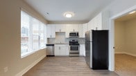 Situated in the heart of Columbus, Ohio, this single-floor space at 223 E Town St offers a clean, contemporary design with thoughtful finishes throughout. The kitchen serves as a standout feature, showcasing crisp white shaker-style cabinetry that extends to the ceiling, providing generous storage. A full suite of stainless steel appliances — including a refrigerator, range, built-in microwave, and dishwasher — equips the space for functional, everyday use. Dark countertops offer a striking contrast against the white cabinetry, while a classic tile backsplash adds texture and a polished finish. Natural light pours in through large windows dressed with horizontal blinds, brightening the space and creating an open, airy atmosphere. Warm-toned hardwood-style flooring runs throughout, adding continuity and a welcoming feel underfoot. The neutral color palette of soft whites and warm beige tones throughout the walls and trim creates a versatile backdrop suited to a variety of uses. The overall design reflects a modern aesthetic with practical, well-appointed details that make the space both functional and visually appealing.