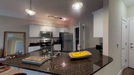 Located at 5541 Bowland Pl in Dublin, Ohio, this single-floor residence offers a well-designed layout with thoughtfully appointed living spaces. The kitchen is a standout feature, showcasing dark granite countertops, white cabinetry, stainless steel appliances including a refrigerator, electric range, and microwave, and a peninsula with an undermount sink and pendant lighting overhead. Track lighting adds a modern touch, and a stacked washer/dryer unit is conveniently located just off the kitchen. The rich hardwood flooring throughout the kitchen and main living areas adds warmth and continuity to the space. The bedrooms are carpeted and offer a cozy, neutral palette with natural light filtering through window blinds adorned with yellow accent valances. Each bedroom provides ample space for full-sized furniture arrangements. The bathroom is generously sized, featuring a dual-sink vanity with dark granite countertops set against white cabinetry, tile flooring, and a walk-in glass-enclosed shower with tile surround and a built-in bench. The overall ambiance throughout the residence is clean and contemporary, with neutral tones, modern finishes, and a cohesive design that balances function and style.