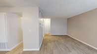 This 1-bedroom, 1-bathroom unit offers a clean, modern layout spread across a single floor. Light wood-look flooring runs continuously throughout the space, complemented by neutral warm-toned walls, crisp white baseboards, and textured ceilings that together create a cohesive and welcoming atmosphere.

The open living area provides a generous, flexible space ideal for both relaxing and entertaining. A hallway connects the main living area to the private spaces beyond. The kitchen features white shaker-style cabinetry, quartz-look countertops, a stainless steel double-basin sink with a brushed nickel faucet, a stainless steel refrigerator, and a dishwasher — offering both style and practicality.

The bedroom is a comfortable, well-sized room with a window that allows natural light to filter in. It includes direct access to a dedicated walk-in closet equipped with wrap-around hanging rods, providing ample storage. The full bathroom is finished in an all-white palette, featuring a single-sink vanity with white cabinetry, a large mirror, and a shower/tub combo. The consistent wood-look flooring extends into the bathroom, tying the overall design together seamlessly throughout the unit.
