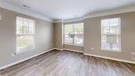 This two-story home in Fort Wayne, Indiana offers a thoughtfully designed layout across two floors. The main level features an open-concept living, dining, and kitchen area united by warm wood-look flooring and neutral taupe walls with crisp white trim and crown molding. Large windows invite abundant natural light, enhancing the airy feel of the living and dining spaces. The kitchen is well-equipped with white cabinetry, granite-style countertops, a full suite of white appliances including a range, built-in microwave, and refrigerator, plus a center island with additional counter space. A staircase with carpet treads leads to the upper level, where all four bedrooms are situated. Each bedroom features plush carpet flooring, ceiling fans, and large windows offering pleasant neighborhood views. The spacious primary bedroom provides a comfortable retreat. Both bathrooms are finished with wood-look tile flooring, white vanity cabinetry, and stone-tone countertops. The home also includes a dedicated laundry area, three hallways for smooth circulation, and an impressive seven closets distributed throughout, offering exceptional storage. The consistent neutral palette and clean finishes create a cohesive, move-in-ready ambiance throughout.