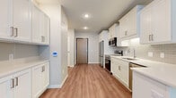 This well-appointed single-floor residence showcases a thoughtfully designed layout with contemporary finishes throughout. The kitchen serves as a standout feature, outfitted with white shaker-style cabinetry, brushed nickel hardware, light quartz countertops, and a classic subway tile backsplash. A full suite of stainless steel appliances — including a range, over-the-range microwave, refrigerator, and dishwasher — provides a fully equipped cooking space. Warm wood-look luxury vinyl plank flooring runs through the kitchen and main living areas, lending a cohesive and modern aesthetic, while a smart thermostat on the wall adds a convenient touch of technology. The bedroom features soft, neutral-toned carpet and benefits from natural light streaming through a window with views of the surrounding streetscape, along with a built-in closet for storage. The full bathroom is finished with a white vanity, quartz countertop, a large mirror, and a combined shower-tub unit with clean white tile surround. Recessed lighting throughout keeps the space bright and functional. The overall design palette of soft grays, whites, and warm wood tones creates a clean, modern, and inviting atmosphere across all rooms.