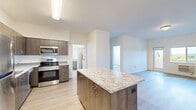 This single-floor, 2-bedroom, 1-bathroom unit offers a well-designed layout with modern finishes throughout. The open-concept kitchen and living area serves as the heart of the space, anchored by a central island with a striking granite countertop and wood-toned cabinetry with gold hardware. The kitchen is fully equipped with stainless steel appliances, including a refrigerator, electric range, microwave, and dishwasher, complemented by ample upper and lower cabinetry and a clean tile backsplash. Light wood-style flooring extends throughout the unit, creating a cohesive and contemporary aesthetic.

The open living area provides a flexible, unobstructed layout with clean white walls and neutral tones. The primary bedroom offers a comfortable footprint and includes a walk-in closet with built-in shelving, as well as a window that frames outdoor views. The second bedroom is bright and functional, featuring its own window for natural light. The shared bathroom includes a wood-toned vanity with granite countertop, a large mirror, and a frosted window for privacy. The unit's consistent use of modern materials and neutral palette creates a clean, functional living environment.