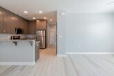 This well-appointed single-floor unit offers a thoughtfully designed layout that blends modern finishes with functional living spaces. Light hardwood flooring flows consistently throughout, tying each room together and creating a bright, cohesive aesthetic.

The entry foyer welcomes residents through a white paneled door with glass accents, flanked by windows fitted with blinds that allow for natural light and privacy. The open-concept kitchen and living area serves as the heart of the unit. The kitchen is equipped with warm-toned wood cabinetry, granite countertops, stainless steel appliances including a refrigerator, gas range, and built-in microwave, as well as a double basin sink. A peninsula with bar seating provides a casual dining option and visually connects the kitchen to the living space.

The unit includes multiple bedrooms, each featuring ceiling fans, neutral gray walls, and windows with outdoor views of the surrounding neighborhood. The rooms offer generous proportions suitable for varied uses.

Two bathrooms serve the unit — one featuring a tub and shower combination with a sliding glass enclosure, and the other a sleek vanity with a granite countertop, undermount sink, and mirrored medicine cabinet. Both bathrooms continue the light hardwood flooring and neutral color palette seen throughout the unit, contributing to its clean and modern overall ambiance.