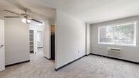 This single-floor unit offers three bedrooms, one bathroom, a kitchen, a hallway, and a dedicated closet space, all within a compact but efficiently arranged footprint. The layout connects rooms through a central hallway, providing clear separation between living and sleeping areas.

The bedrooms are carpeted throughout and each features a ceiling fan with integrated lighting. The generously sized primary bedroom offers notable floor space relative to the overall unit. Two additional bedrooms include closets with hanging rods and shelving, and several windows allow natural light to enter. One bedroom features dual windows on adjacent walls, enhancing brightness.

The kitchen is a narrow galley-style space finished with warm wood-toned laminate flooring and light natural wood cabinetry extending to the ceiling. It is equipped with a black refrigerator and a gas range, along with a window providing ventilation and natural light.

The bathroom features a full-size soaking tub with an overhead window, a wood-vanity with a single sink, a wall-mounted mirror cabinet, and classic mosaic tile flooring in a neutral pattern. Clean white walls and a light fixture above the vanity complete the space.

Overall, the unit presents a straightforward, functional design with consistent neutral tones throughout.
