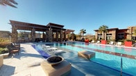 This outdoor pool facility offers a well-appointed aquatic retreat designed for relaxation and recreation. The centerpiece is a generously sized swimming pool with crystal-clear blue water, complemented by a separate spa or secondary pool area visible nearby. In-pool platform loungers allow residents to relax directly in the water, while a shallow entry zone adds to the resort-style experience. Decorative fire bowls accent the pool deck, providing both ambiance and visual interest.

A striking covered pergola structure anchors one side of the pool area, featuring robust stone columns and a slatted wood-tone roof that provides shade and a defined social gathering space. Ceiling fans are mounted within the pergola, enhancing comfort during warmer months. Additional seating areas with lounge chairs and umbrellas are arranged around the pool deck for sunbathing and leisure.

Lush palm trees and mature landscaping frame the space, reinforcing the resort atmosphere. The surrounding multi-story residential building wraps around the pool area, creating a sheltered and private courtyard feel. Access to the pool is provided through a dedicated entry point with wood-framed glass doors, accompanied by clearly posted pool rules. The open-air design maximizes natural light and sky views throughout the day.