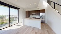 Located at 101 Manchester Rd in Richmond, VA, this contemporary two-floor residence showcases a clean, modern design with light hardwood flooring, crisp white walls, and large black-framed windows that flood every room with natural light. The open-concept kitchen is a standout feature, equipped with rich dark wood cabinetry extending to the ceiling, quartz countertops, a central island with an undermount sink, and a full suite of stainless steel appliances. Sliding glass doors lead to a private balcony, offering outdoor views directly from the main living area. A dramatic living space features soaring double-height ceilings with clerestory windows above, creating an airy, light-filled atmosphere. Additional bedrooms are generously proportioned, with floor-to-ceiling windows and ceiling fans. The bathrooms are finished to a high standard, featuring large-format tile flooring, dark wood floating vanities with white quartz countertops, and backlit mirrors. The primary bathroom includes a dual-sink vanity and a tall vertical window for natural light. A full tub-shower bathroom serves additional occupants. The entry foyer provides a clean transition into the home, complementing the cohesive, minimalist aesthetic found throughout this well-appointed Richmond residence.