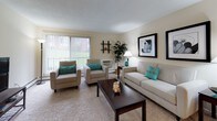 This one-bedroom residence is thoughtfully arranged across a single floor, offering a functional and comfortable layout. The living room serves as the centerpiece of the home, featuring plush wall-to-wall carpeting, neutral-toned walls, and large sliding glass doors with vertical blinds that invite natural light and provide views of the surrounding greenery. The generous room size accommodates both a seating and media area with ease.

Adjacent to the entry, a dedicated dining nook is illuminated by a ceiling fan with a light fixture, providing an intimate space for meals. A sliding mirrored closet near the entry offers convenient storage. The kitchen is equipped with warm oak cabinetry extending to the ceiling, laminate countertops, a stainless steel sink, and white appliances including a refrigerator and range, all set above dark hardwood-style flooring.

The bedroom is a quiet retreat with soft carpeting, baseboard heating, and windows with outdoor views. Two mirrored sliding closet doors add depth while maximizing storage. The bathroom features white subway tile walling, a vanity with a wide mirror, patterned tile flooring, and dark wood-style flooring at the entry, completing the unit's cohesive design.