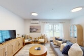 Located at 8 Admiral Harry Rich Dr in Brunswick, Maine, this well-appointed two-bedroom, two-bathroom residence offers a thoughtfully designed single-floor layout with a bright, coastal aesthetic throughout. Light wood-look flooring flows seamlessly across the main living areas, complementing the clean white walls and modern finishes.

The open-concept kitchen and living room form the heart of the home. The kitchen is equipped with stainless steel appliances, including a range, microwave, refrigerator, and dishwasher, alongside rich taupe cabinetry and a light quartz peninsula with bar seating — ideal for casual dining. The spacious living and dining area is generously sized, accommodating both a full dining set and a comfortable lounge area, with windows providing natural light and views of the surrounding neighborhood.

The primary bedroom features soft blue-grey walls, a large window, and ample space for a seating area, offering a serene retreat. A closet with built-in shelving and hanging storage provides excellent organization. The second bedroom is equally versatile, suitable as a guest room or home office. Both bathrooms are finished with dark wood vanities, white countertops, and light wood-look flooring, with one featuring a full tub and shower combination.