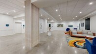 Located at 55 Tunxis Ave in Bloomfield, CT, this generously sized single-floor commercial space offers an open, airy layout with a refined yet contemporary aesthetic. Polished concrete floors run throughout, reflecting recessed lighting and contributing to the bright, clean atmosphere. Crisp white walls are accented with classic wainscoting panels, lending an air of sophistication to the corridors and gathering areas.

The space features a welcoming main hall that opens into a spacious lounge area, complete with a sleek modern fireplace set against a bold dark accent wall, colorful area rugs, and a curated mix of seating. Slat-wrapped structural columns add a warm, natural wood element that contrasts beautifully with the otherwise minimalist palette. Artwork is thoughtfully displayed throughout, transforming the corridors into gallery-like passages.

A grand wooden staircase with ornate detailing serves as a striking architectural focal point, drawing the eye upward beneath a skylight that introduces natural light. Glass-paneled entry doors along one wing invite views to the outdoors. Drop ceilings with recessed lighting ensure consistent illumination across the entire floor. The overall ambiance is polished, versatile, and well-suited for professional or community-oriented use.