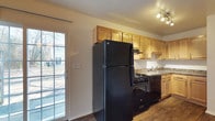 This two-floor residence offers a clean, functional layout designed for comfortable everyday living. The main living areas are finished with neutral-toned carpet, contributing to a warm and quiet atmosphere throughout. White walls and standard ceiling heights create a bright, open feel, while ceiling-mounted HVAC vents ensure year-round climate control. Closet space is thoughtfully integrated, with louvered bi-fold doors providing convenient storage access directly off the living areas.

The kitchen is a practical and well-equipped space, featuring warm honey-toned wood cabinetry that extends to the upper walls for generous storage capacity. Black appliances—including a full-size refrigerator, gas range, and dishwasher—offer a cohesive, modern contrast against the cabinetry. Stone-look countertops and a stainless sink complete the functional workspace, while track lighting overhead ensures clear visibility. A glass door in the kitchen floods the space with natural light and provides a direct view to the exterior, enhancing the sense of openness. The kitchen flooring transitions to hardwood, adding a durable and attractive surface underfoot. Overall, the space presents a straightforward and move-in-ready layout suited for a range of lifestyles.