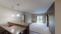 Located at 1290 County Road F W in Arden Hills, Minnesota, this single-floor residence offers a thoughtfully designed open-concept layout. The kitchen is equipped with dark espresso cabinetry, granite countertops, stainless steel appliances, and a tile floor. Pendant lighting hangs above the extended breakfast bar, which opens directly into the living area — creating a seamless flow between cooking and entertaining spaces. The living room features plush carpeting and a sliding glass door that leads to a private balcony overlooking a lush, tree-lined outdoor area, bringing in generous natural light. Two carpeted bedrooms each include ceiling fans, wall-unit air conditioning, and windows with blinds that allow for natural light and privacy. A spacious walk-in closet with wire shelving provides ample storage in the primary bedroom. The bathroom is finished with granite countertops, dark cabinetry, a large mirror with overhead lighting, and a full tub-shower combination. Throughout the residence, neutral warm tones, dark trim accents, and consistent finishes create a cohesive and functional living environment suited for everyday comfort.