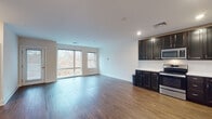 Located at 260 Highland Corporate Dr in Cumberland, Rhode Island, this modern single-floor unit offers a well-designed, open-concept layout ideal for comfortable everyday living. The expansive living and dining area is anchored by rich, dark hardwood flooring and bathed in natural light through large windows that frame views of the surrounding wooded landscape. The kitchen flows seamlessly into the living space and is outfitted with dark espresso cabinetry, white countertops, a subway tile backsplash, and a full suite of stainless steel appliances including a range, microwave, dishwasher, and refrigerator. Recessed lighting adds a clean, contemporary finish overhead. The bedrooms feature plush wall-to-wall carpeting and generously sized windows that bring in abundant natural light. One bedroom includes a large walk-in closet with wire shelving, offering excellent storage capacity. The two bathrooms are finished with classic black-and-white mosaic tile flooring and white vanities; one includes a walk-in shower while the other features a full soaking tub. A dedicated in-unit laundry closet with a stacked washer and dryer adds everyday convenience. Throughout, the unit maintains a clean, neutral palette that is both modern and inviting.