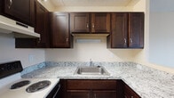 Located at 109 Broad St in Weymouth, Massachusetts, this single-floor unit offers a well-appointed and functional layout. The kitchen is a standout feature, showcasing rich dark-brown cabinetry with brushed nickel hardware, granite countertops with a classic white and grey veining pattern, a stainless steel sink, and an electric range — providing ample storage and a clean, modern aesthetic.

The living area is generously sized, finished with wall-to-wall carpeting and a ceiling fan with integrated lighting. A sliding glass door opens to an outdoor balcony or patio, allowing natural light to fill the space and providing views of the surrounding greenery. Baseboard heating runs along the perimeter of the room for year-round comfort.

The bedroom features the same comfortable carpeted flooring, a ceiling fan, natural light from a window with blinds, and a built-in closet with a sliding door and hanging rod for convenient storage.

The bathroom is fully equipped with a tiled tub and shower combination fitted with grab bars and a handheld showerhead, a toilet, a wood-toned vanity with an integrated sink, a medicine cabinet mirror, and durable tile flooring. The neutral, warm tones throughout the unit create a cohesive and welcoming atmosphere.