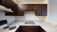 Located at 109 Broad St in Weymouth, Massachusetts, this single-floor unit offers a well-appointed and functional layout. The kitchen is a standout feature, showcasing rich dark-brown cabinetry with brushed nickel hardware, granite countertops with a classic white and grey veining pattern, a stainless steel sink, and an electric range — providing ample storage and a clean, modern aesthetic.

The living area is generously sized, finished with wall-to-wall carpeting and a ceiling fan with integrated lighting. A sliding glass door opens to an outdoor balcony or patio, allowing natural light to fill the space and providing views of the surrounding greenery. Baseboard heating runs along the perimeter of the room for year-round comfort.

The bedroom features the same comfortable carpeted flooring, a ceiling fan, natural light from a window with blinds, and a built-in closet with a sliding door and hanging rod for convenient storage.

The bathroom is fully equipped with a tiled tub and shower combination fitted with grab bars and a handheld showerhead, a toilet, a wood-toned vanity with an integrated sink, a medicine cabinet mirror, and durable tile flooring. The neutral, warm tones throughout the unit create a cohesive and welcoming atmosphere.